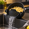 Black clip-on pot strainer draining pasta over a kitchen sink